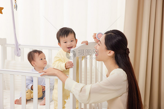 妈妈和婴儿床上开心玩耍的双胞胎图片