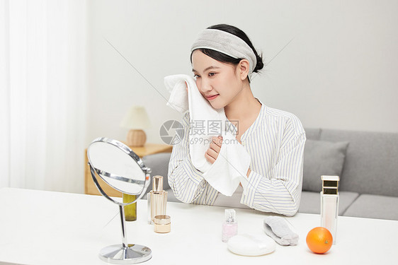 镜子前用毛巾擦拭脸颊的年轻女孩图片
