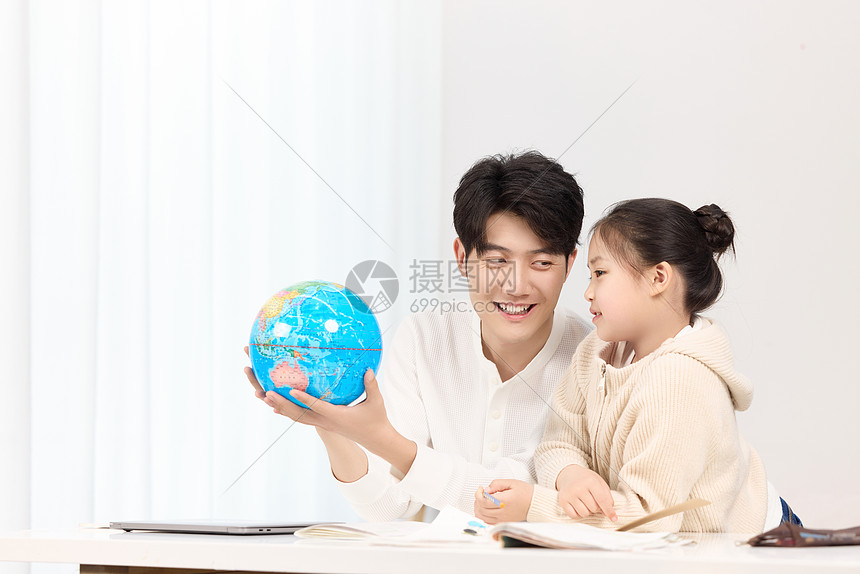 正拿着地球仪给女儿讲解的年轻爸爸图片