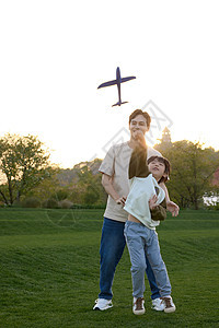 户外草坪上正在教孩子玩玩具飞机的年轻父亲图片