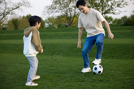 在户外草坪上踢足球的父子俩图片