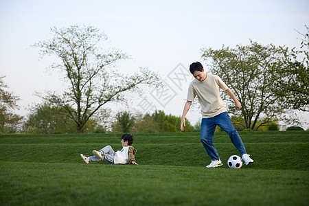 小男孩玩球躺在草坪上的小男孩和在旁边玩球的父亲背景