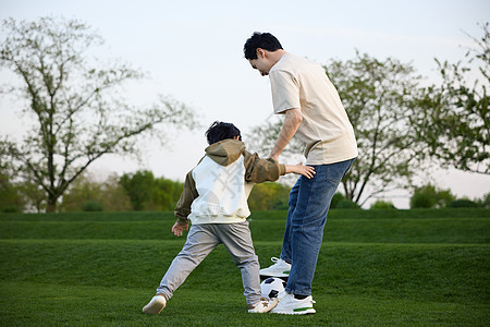 和爸爸在草坪上玩足球的小男孩图片