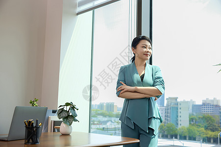 女白领双臂交叉站在办公室窗边图片