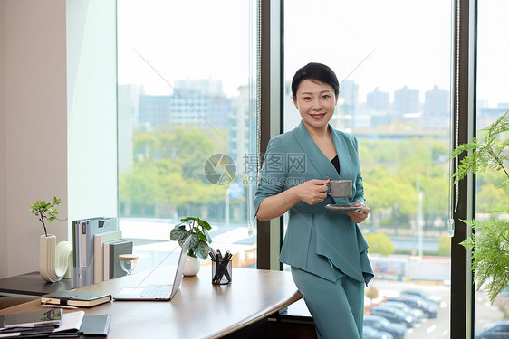 女白领靠着办公桌喝咖啡图片