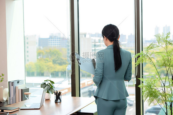 女白领拿着文件夹站在办公室的窗边图片