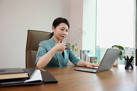 女白领坐在办公室电脑前喝咖啡背景图片