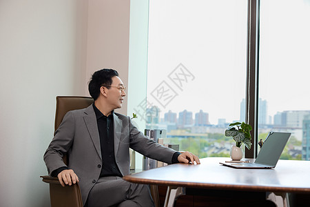 一位男白领坐在办公室看向窗外图片