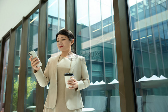 女白领在公司走廊拿着咖啡对手机笑图片