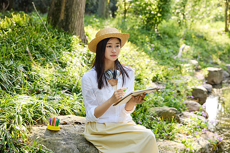 坐在小溪边石头上画画的美女图片