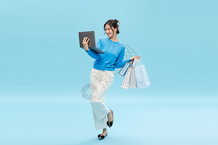 一边购物一边抱着电脑开心办公的美女图片