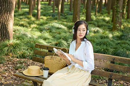 美女坐在户外长椅上听歌看书图片