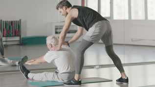 健身教练帮助退休男子在健身俱乐部里进行伸展运动视频素材