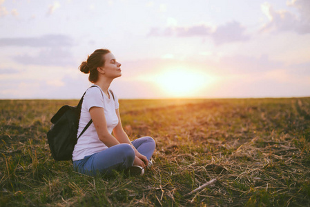 年轻女人放松在夏季室外的夕阳的天空。人考