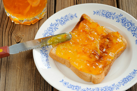 木制的背景上的橙色果酱土司面包照片