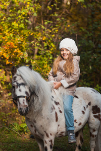 美丽小姑娘坐在一匹小马在秋天的公园