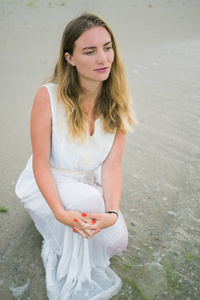 生活方式女人坐在一条白色的裙子在海洋海岸垂直拍摄