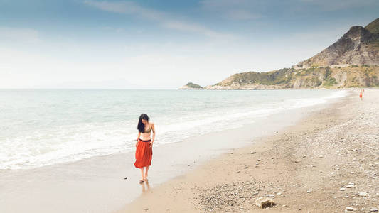 年轻女子独自在赤脚走在海岸边