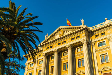 国会大厦在巴塞罗那与棕榈树 旗帜和温暖的阳光
