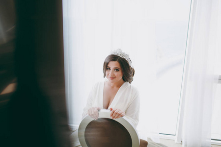 新娘穿着白色绸缎睡衣的黑发坐在窗户旁边
