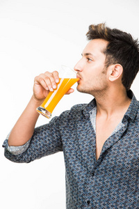 年轻英俊的印度裔男子于休闲衬衫饮酒或充满了新鲜的橙汁或加气早饭喝一杯