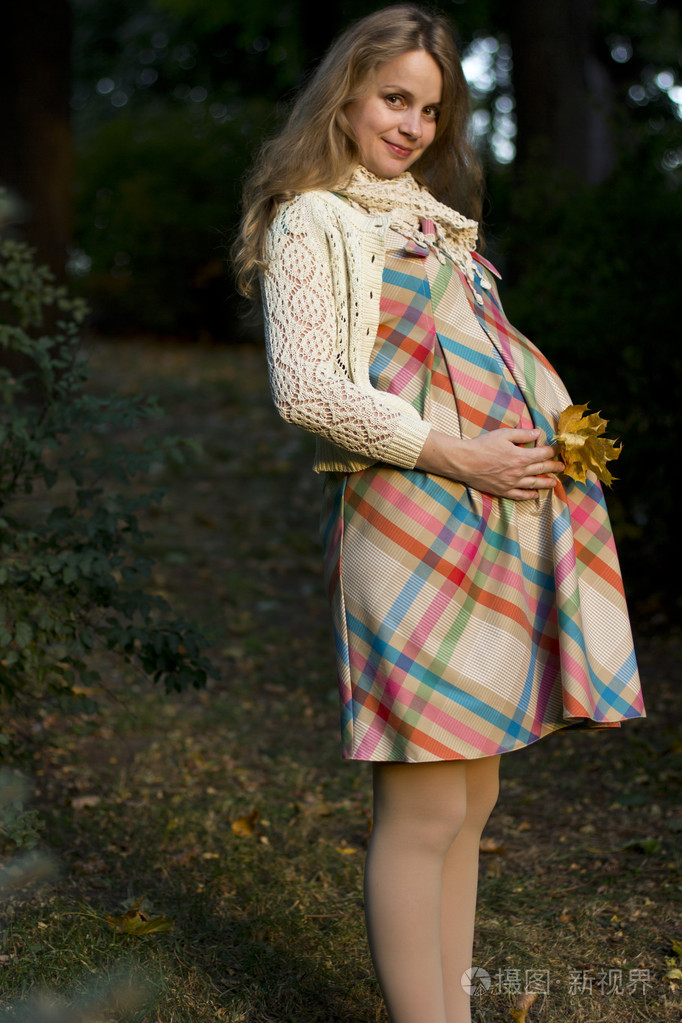 美丽开朗怀孕金发美女走在公园里.一个年轻的怀孕女人的画像照片-正版