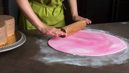 女人用擀面杖准备粉色翻糖蛋糕装饰，手详细