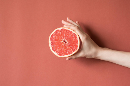 一个年轻的女人，牵着红色的葡萄柚的手。健康食品的概念