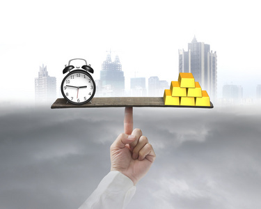 时钟和黄金在支持通过手指的跷跷板上保持平衡照片