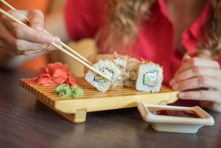 女孩吃寿司卷用木制筷子和摩卡他们酱油中的日本食品保持照片