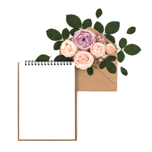 平躺的工作区。婚礼笔记本请柬 粉色玫瑰和白色背景上绿色的叶子。顶视图顶视图