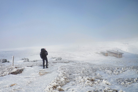 与大背包和雪雾雪路上走向的独自旅游。国家公园在意大利阿尔卑斯山公园。守旧者冬天的天气。在背景中的小屋