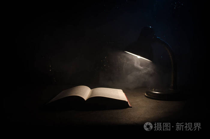 打开的书附近发光台灯上深色背景, 灯和烟雾背景上已打开的书.超现实
