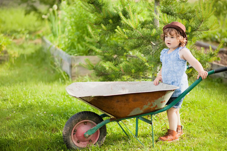 金发碧眼的小孩女孩与一辆手推车在花园里