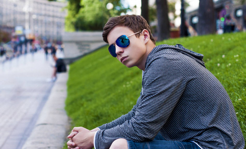 英俊的年轻男子，戴着眼镜坐在草地上