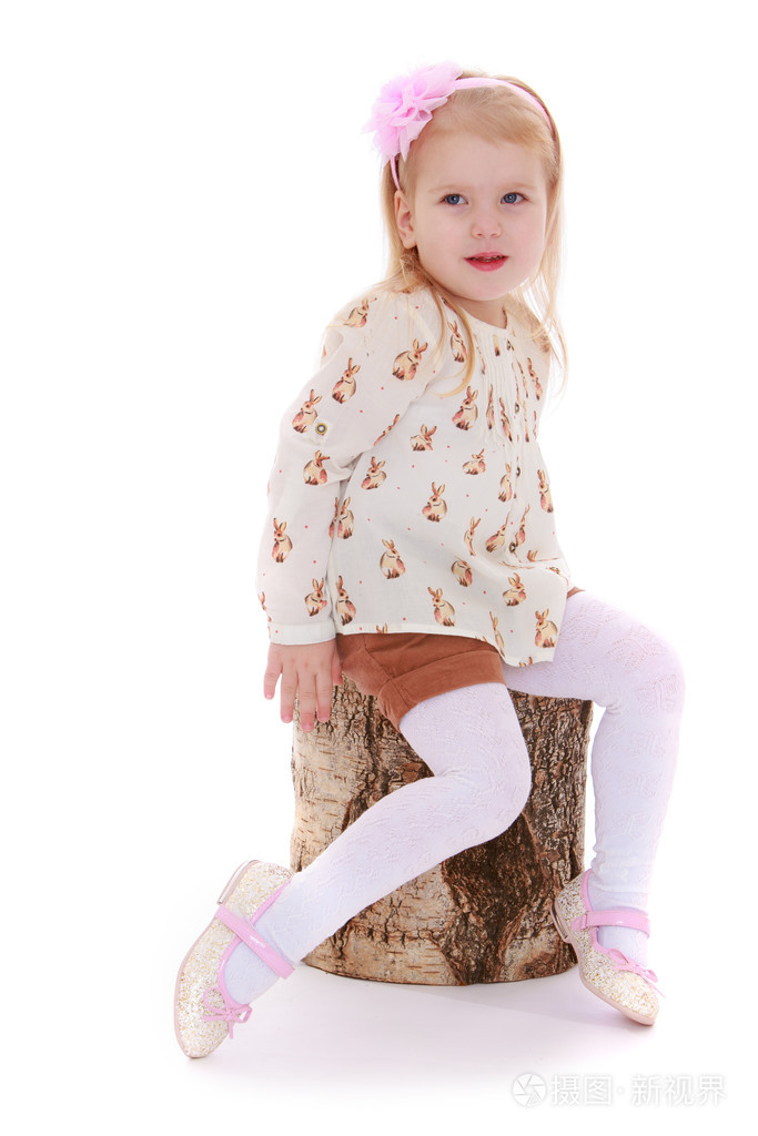 时尚的小女孩正坐在一个树桩上