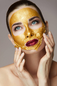 面部皮肤的化妆品。女性与金面具抚摸的脸