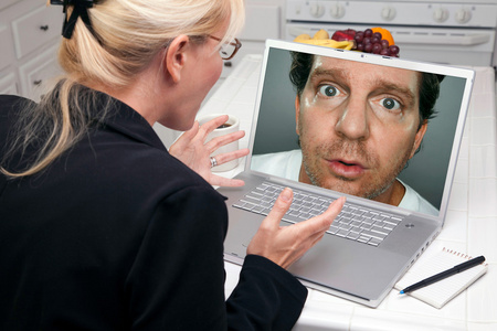 厨房里的震惊女人用笔记本电脑屏幕上的陌生男人