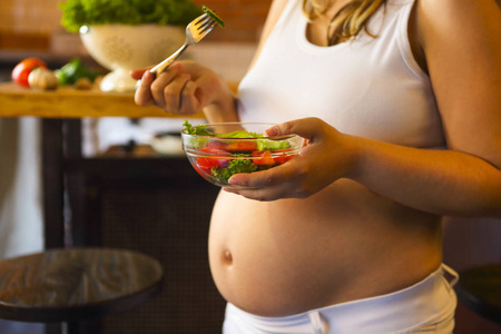 年轻孕妇在厨房吃新鲜的蔬菜沙拉