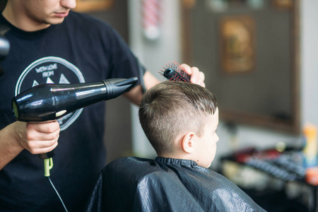 设计师剃刀在理发店剪头发的小男孩坐在椅子上照片