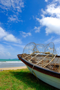 向海景的绿色草地上的渔夫船滞留在晴天和阴天的蓝色天空背景