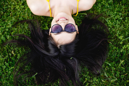 快乐年轻的黑发女人，躺在草地上，顶视图的太阳镜