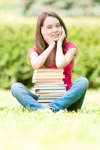 快乐的学生女孩坐在旁边堆书