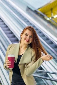 女孩微笑着，拿着杯咖啡附近地铁自动扶梯