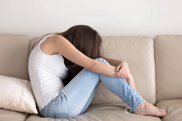 郁闷的女孩坐在沙发上和拥抱的膝盖