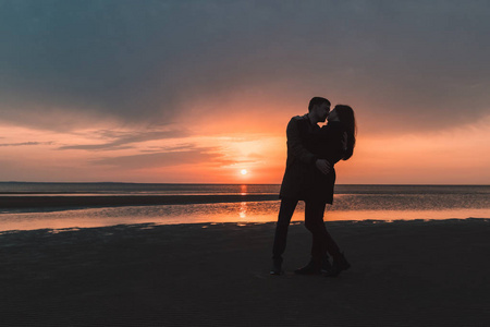 年轻恩爱的夫妻轻轻吻在日落时分在海边，在秋天