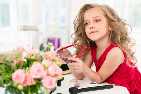 一个小女孩用化妆品。她是在母亲的卧室里，坐在靠近镜子