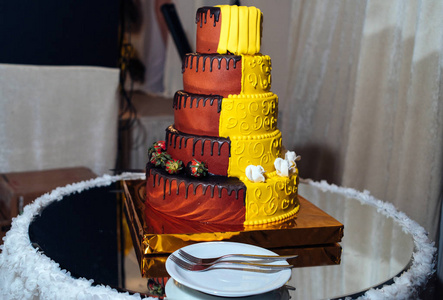 圆形多层黄色和棕色婚礼蛋糕与草莓, 玫瑰和巧克力糖衣。盘子和叉子在蛋糕附近