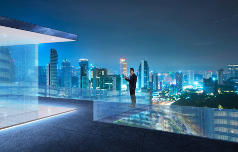 生意人使用数字设备站立在现代屋顶与美丽的城市天际, 夜场面
