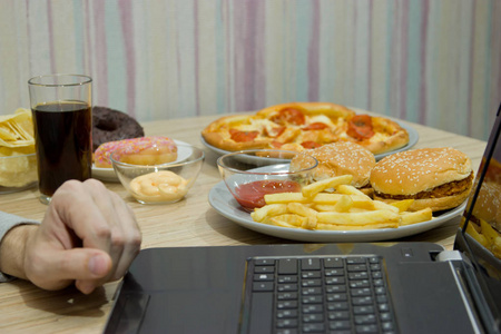 一个人在电脑前工作,吃快餐.不健康食品: 埠照片